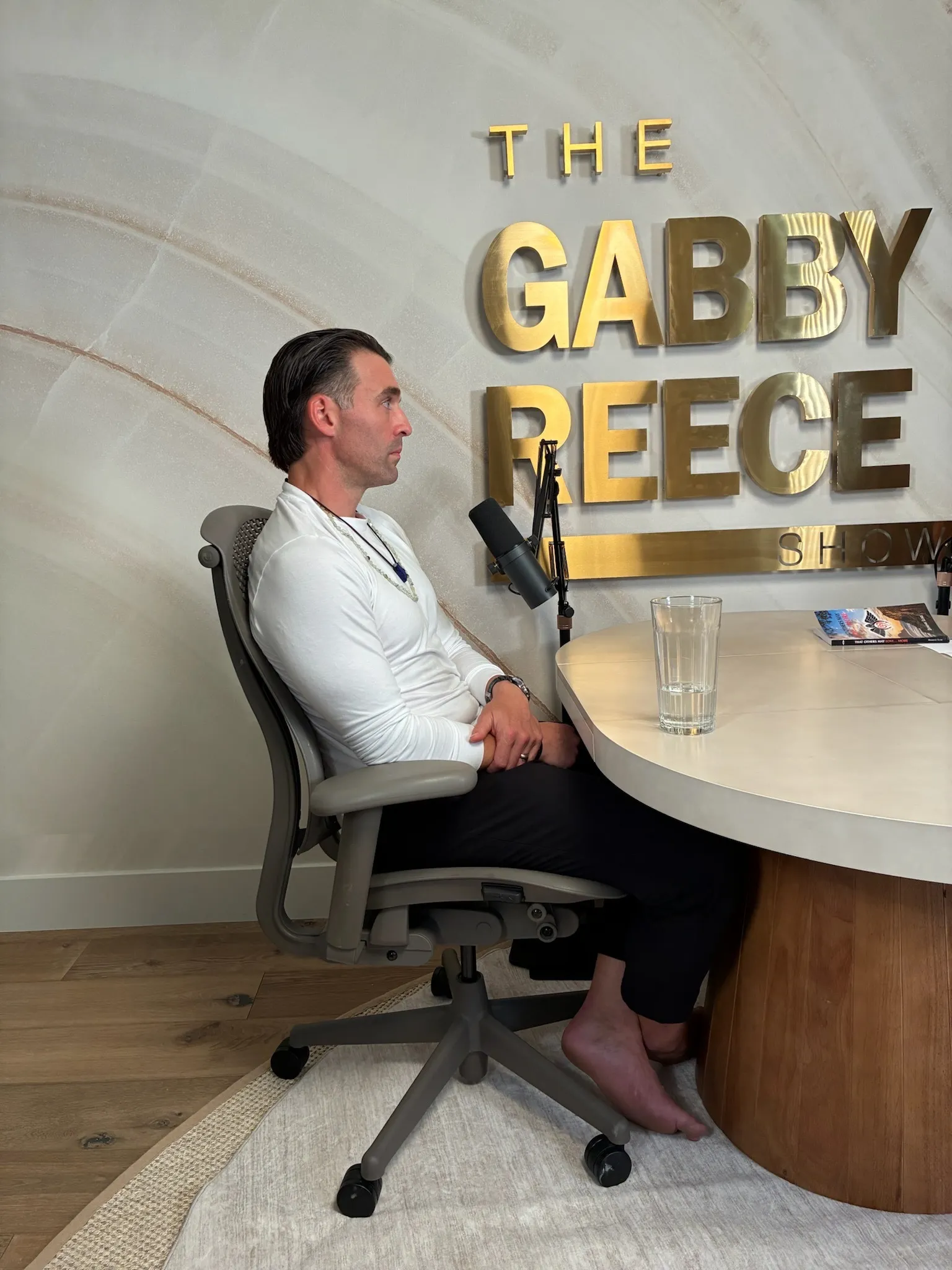 Dominic Luke seated at a microphone on The Gabby Reece Show